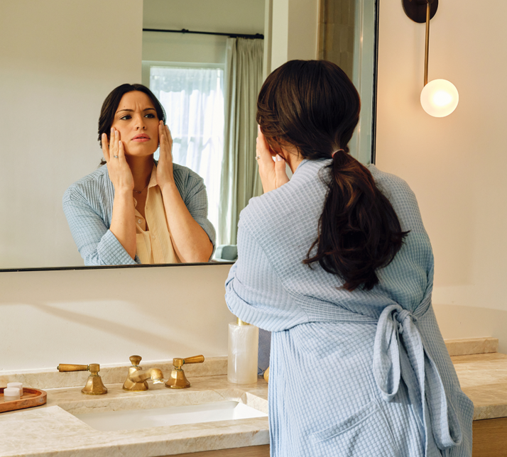 Une femme regarde sa peau devant le miroir de la salle de bain